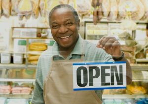 smiling man holding a sign that the business is open thanks to small business grants